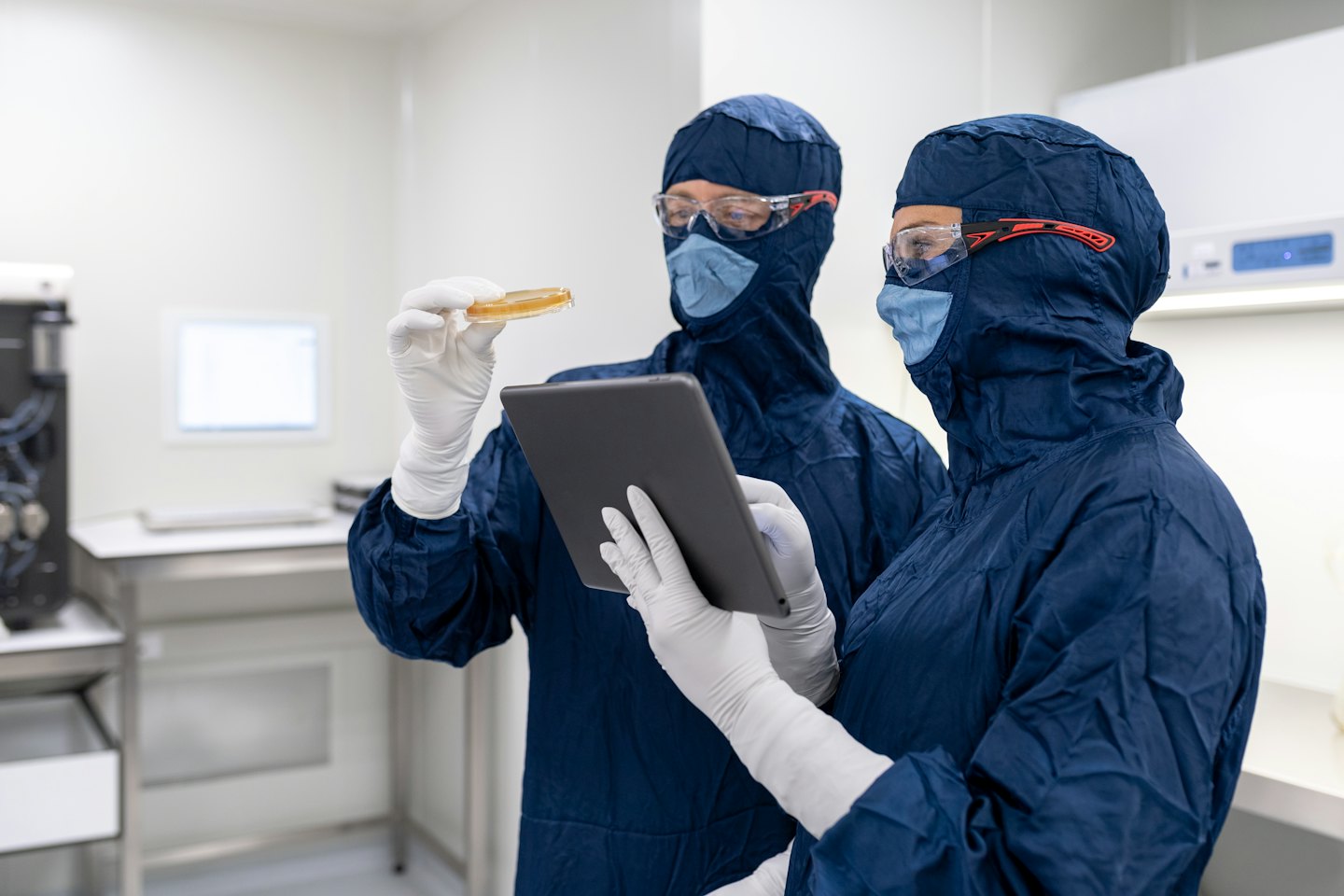 Scienziati in tute da camera bianca esaminano una capsula di Petri e un tablet.
