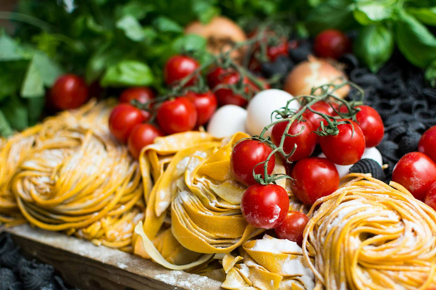 Ingredienti freschi per cucinare, tra cui pasta, pomodori, basilico e uova.